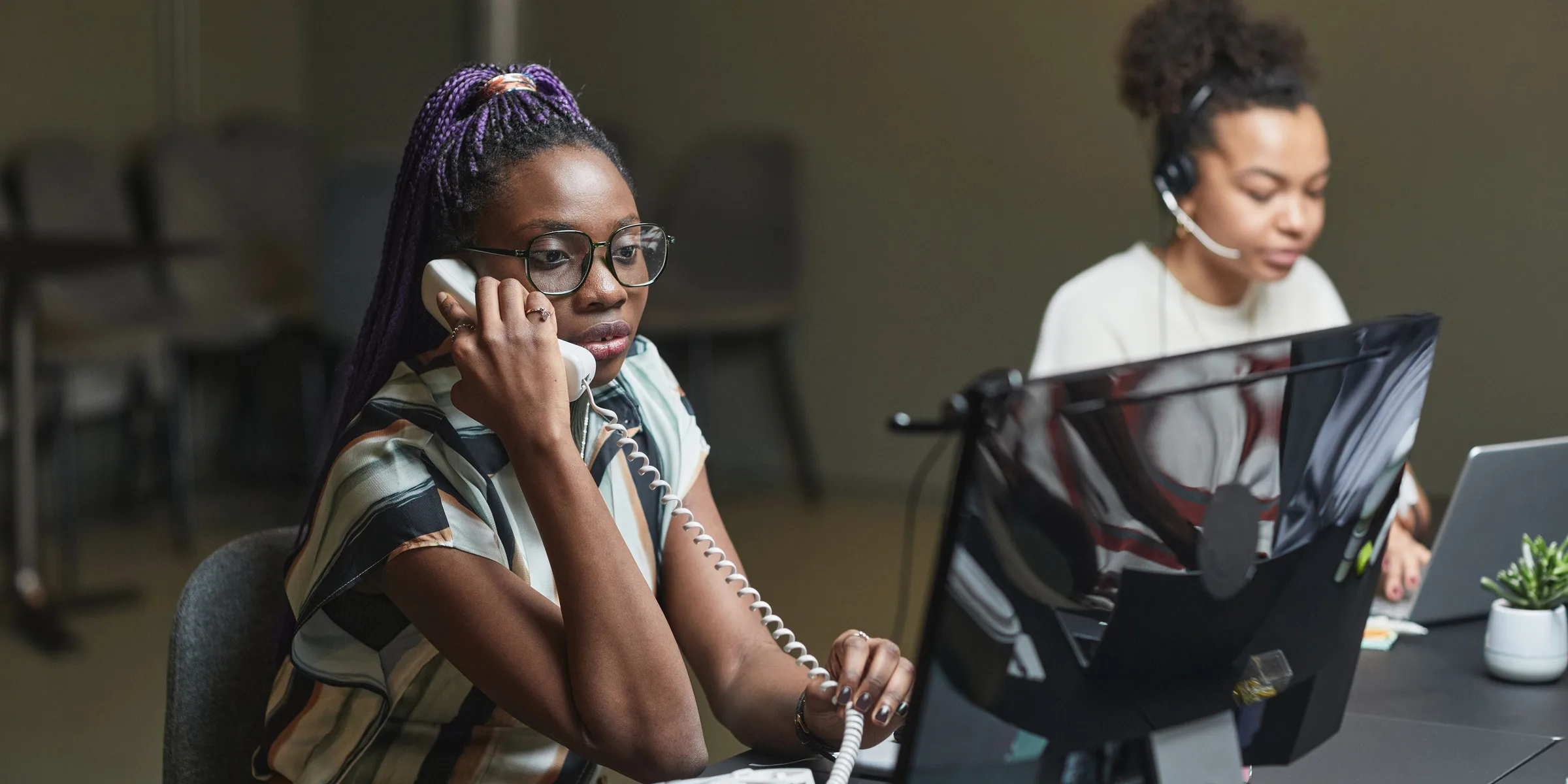 Two service desk staff taking customer calls, one on a desk phone